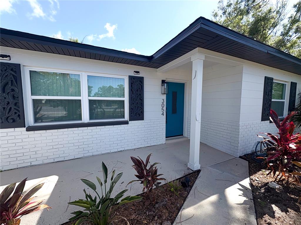 The exterior of a white brick house features a blue front door and dark shutters — 3054 ADRIAN AVENUE, LARGO, FL