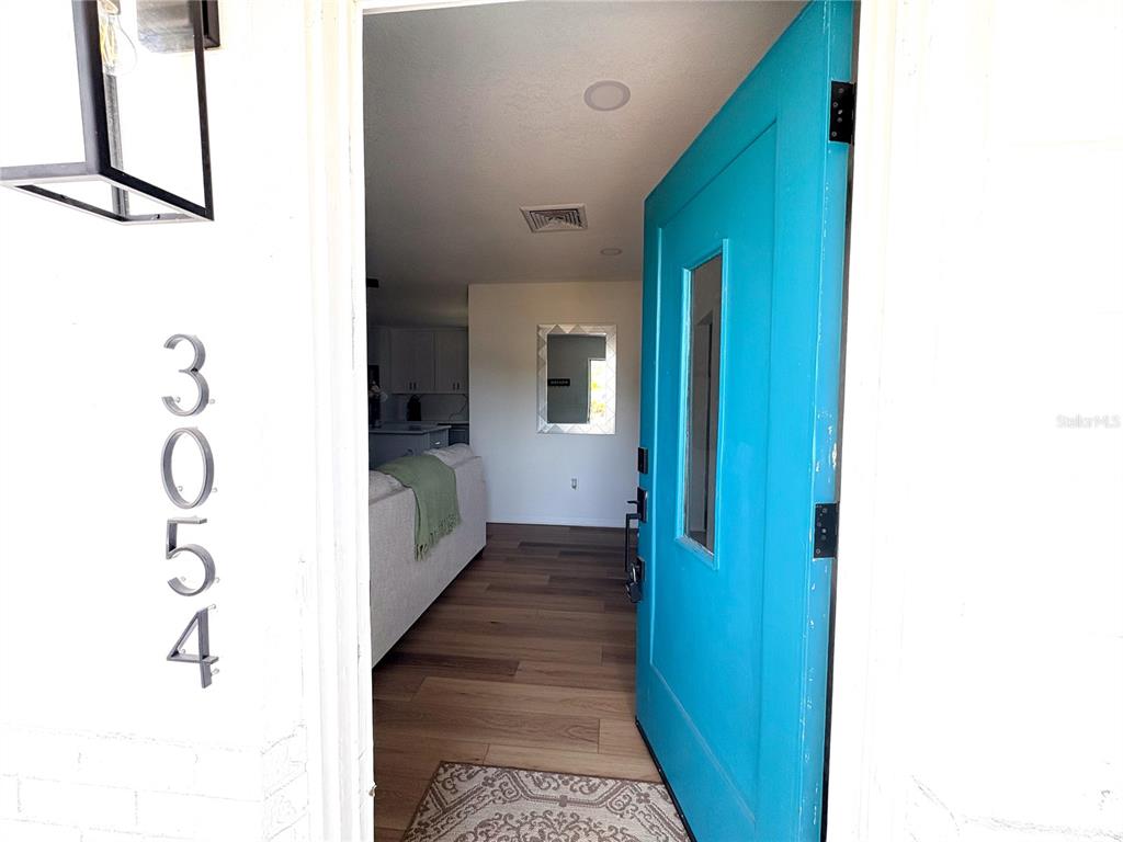 A bright blue front door opens into a home interior with wood-look flooring — 3054 ADRIAN AVENUE, LARGO, FL