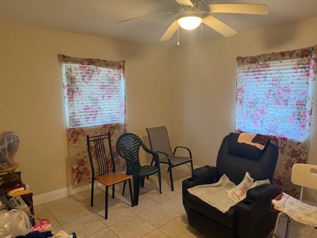 A room with tile floors, a ceiling fan, two windows with floral curtains, and several chairs — 2108 WOLF ROAD, ORLANDO, FL