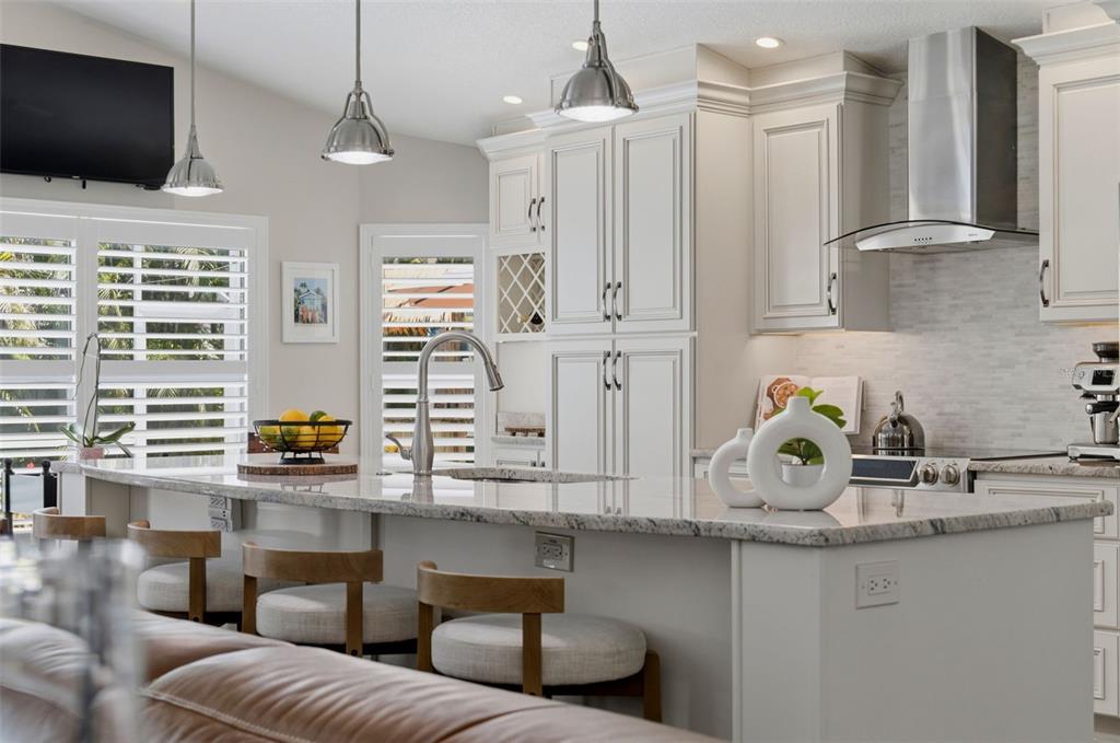 A modern kitchen features white cabinetry, a granite island with bar seating, and pendant lighting — 631 DE SOTO DRIVE, TIERRA VERDE, FL