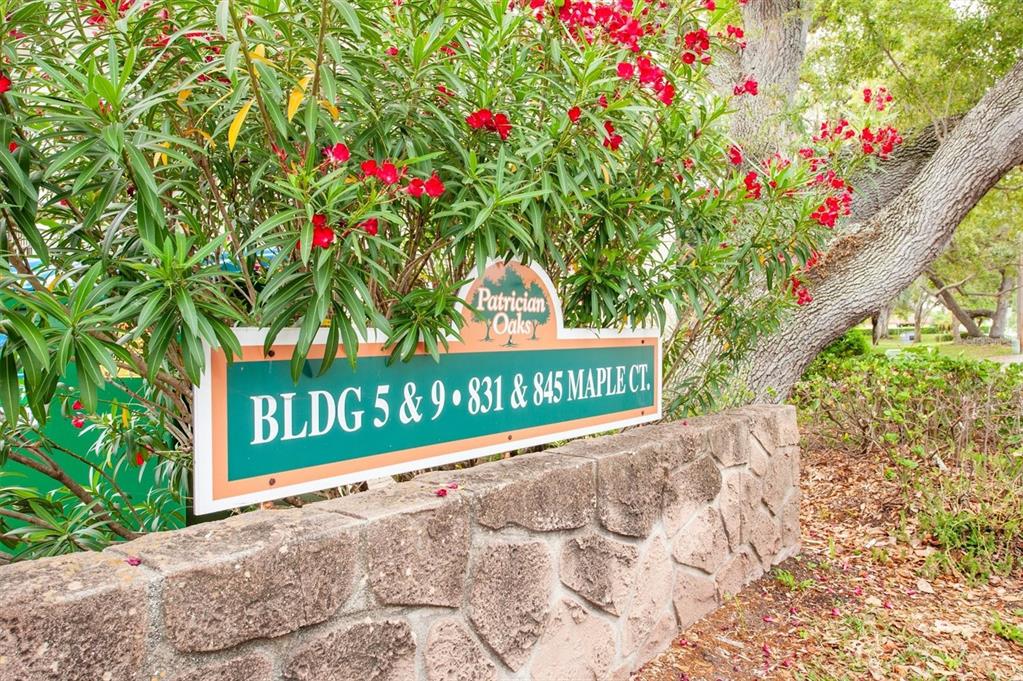 A stone sign for Patrician Oaks stands in front of a flowering oleander bush — 845 MAPLE COURT UNIT 103, DUNEDIN, FL