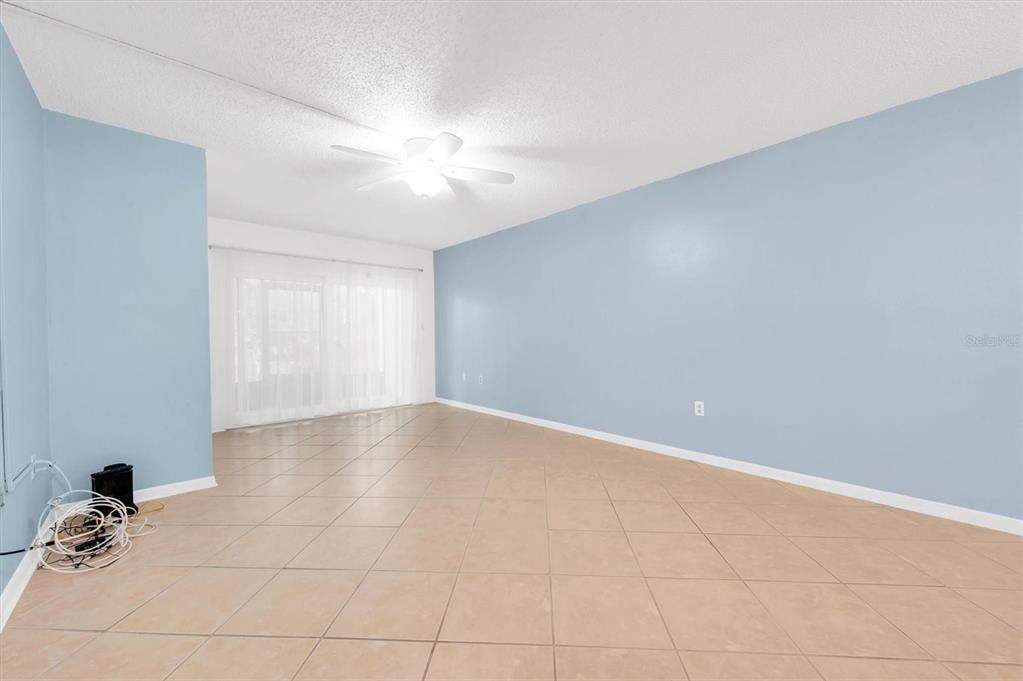 An empty room with light blue walls, beige tile flooring, and a ceiling fan — 845 MAPLE COURT UNIT 103, DUNEDIN, FL