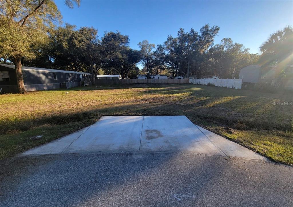 A concrete driveway apron leads to a large, grassy, vacant residential lot with surrounding trees — 325 DONALD LANE, WINTER HAVEN, FL