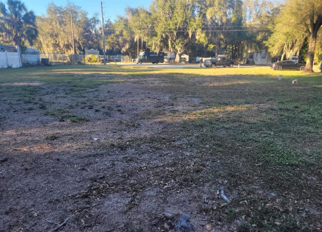 A flat, grassy vacant lot with scattered dirt patches and trees in the background — 325 DONALD LANE, WINTER HAVEN, FL