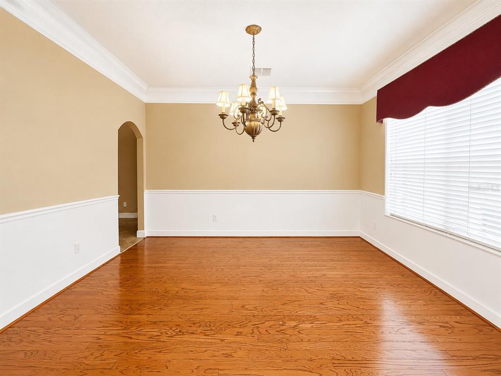 An empty dining room with hardwood floors, white wainscoting, tan walls, and a central chandelier — 8650 TARA OAKS COURT, ORLANDO, FL