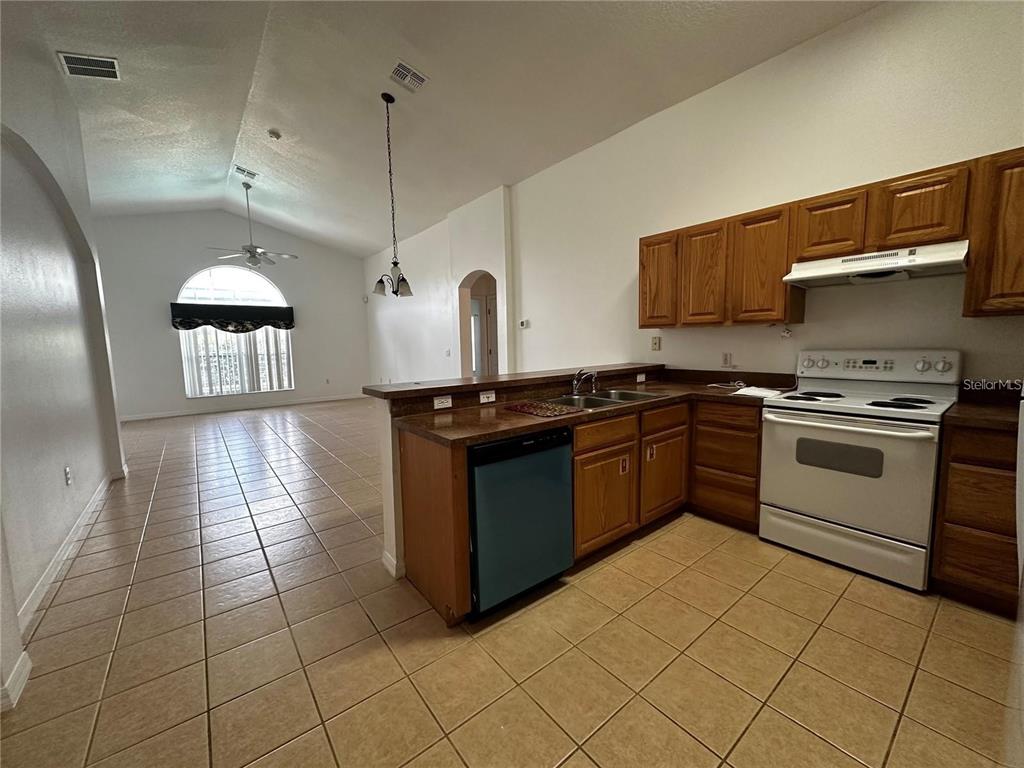 A kitchen with oak cabinets and tile flooring opens into a living area with vaulted ceilings — 4795 CUMBRIAN LAKES DRIVE, KISSIMMEE, FL