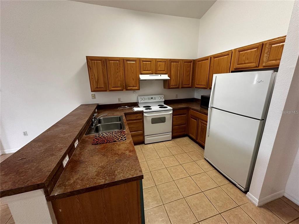 A kitchen features wood cabinets, brown countertops, white appliances, and tan tile flooring — 4795 CUMBRIAN LAKES DRIVE, KISSIMMEE, FL