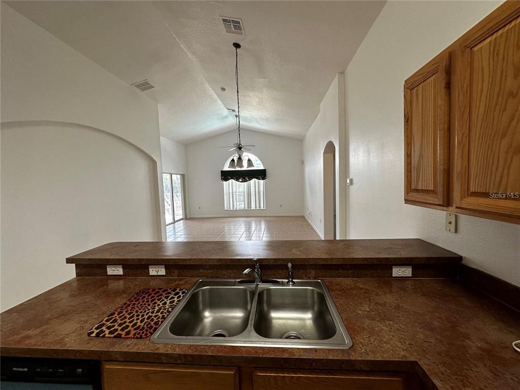 A kitchen sink with a brown countertop overlooks an open-concept living area with vaulted ceilings — 4795 CUMBRIAN LAKES DRIVE, KISSIMMEE, FL