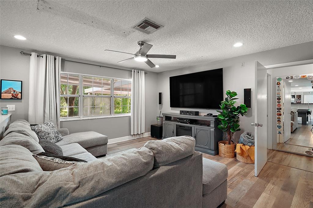 A living room features a gray sectional sofa, a large television, and wood-look flooring — 705 SUMMIT COURT, MOUNT DORA, FL