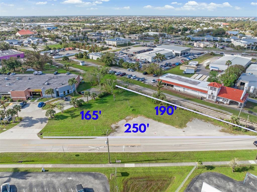 An aerial view shows a vacant, grassy commercial lot bordered by a road and railroad tracks — 1013 TAYLOR ROAD, PUNTA GORDA, FL