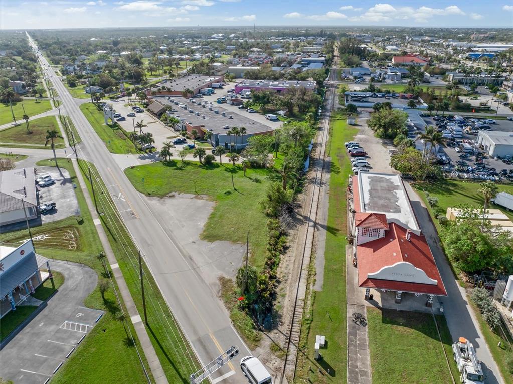 An aerial view shows a road, railroad tracks, and commercial buildings in a suburban area — 1013 TAYLOR ROAD, PUNTA GORDA, FL