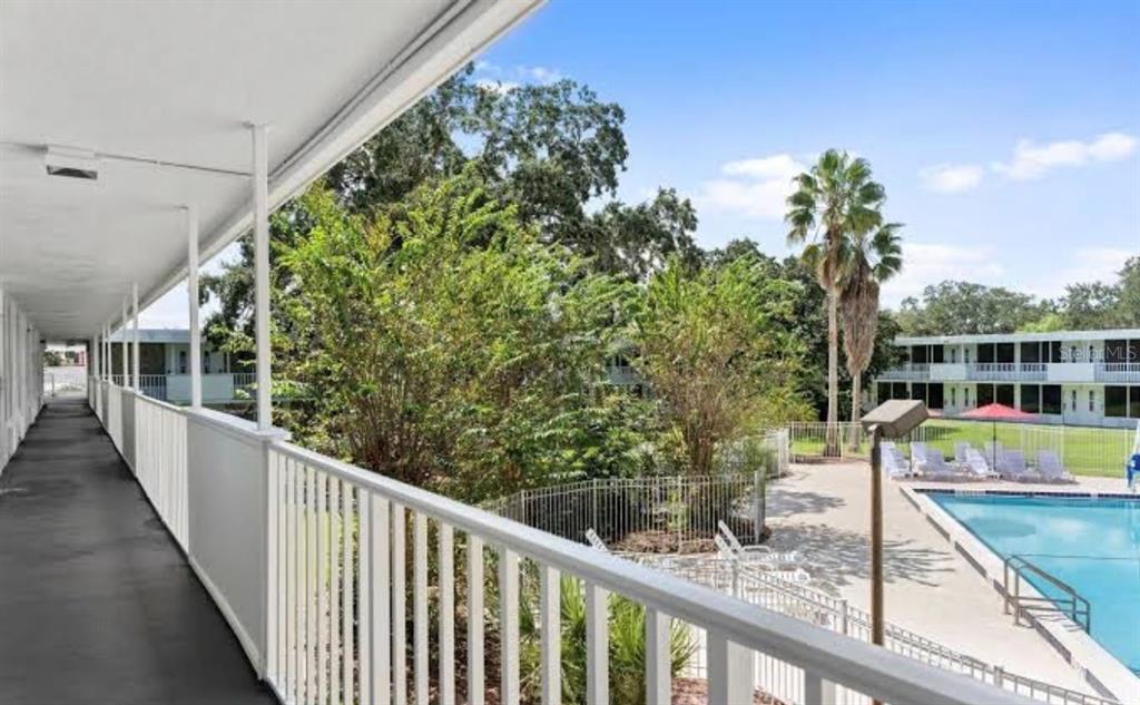 An elevated outdoor walkway overlooks a swimming pool area surrounded by trees and apartment buildings — 2930 POLYNESIAN ISLE BOULEVARD UNIT 223, KISSIMMEE, FL