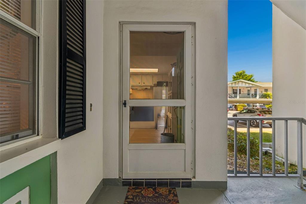 A white storm door leads into a home, viewed from a covered porch with railings — 200 GLENNES LANE UNIT 112, DUNEDIN, FL