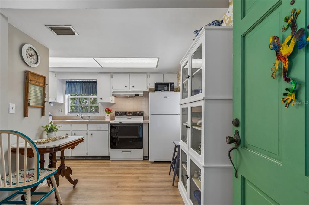 A kitchen with white cabinets, a white refrigerator, a dining table, and a green door — 200 GLENNES LANE UNIT 112, DUNEDIN, FL