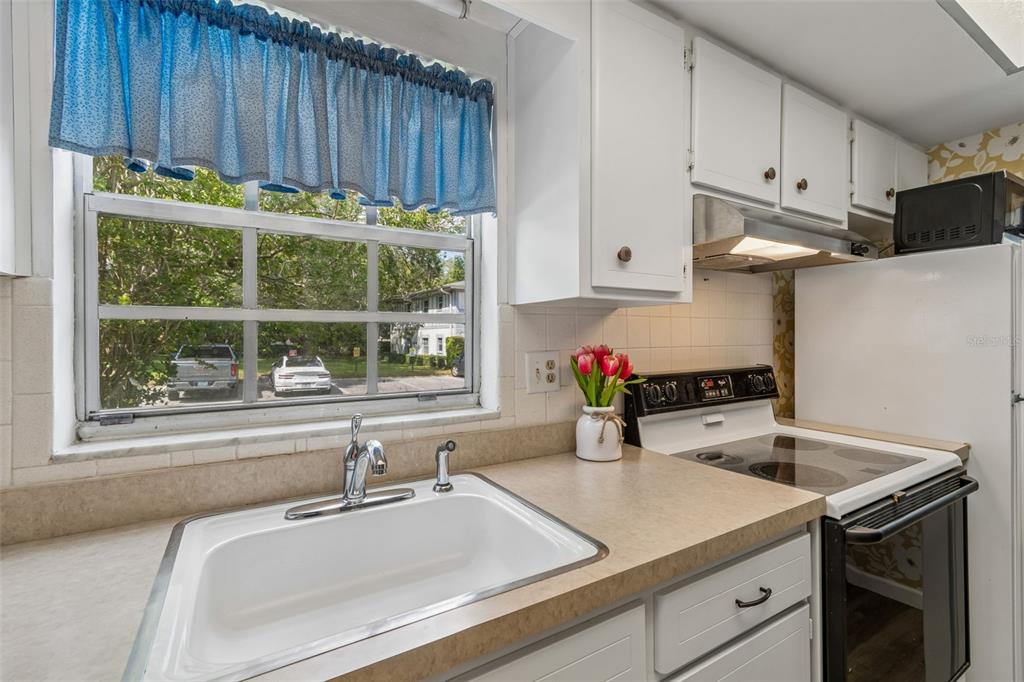 A kitchen with white cabinets, a white sink, a window, and a black electric stove — 200 GLENNES LANE UNIT 112, DUNEDIN, FL