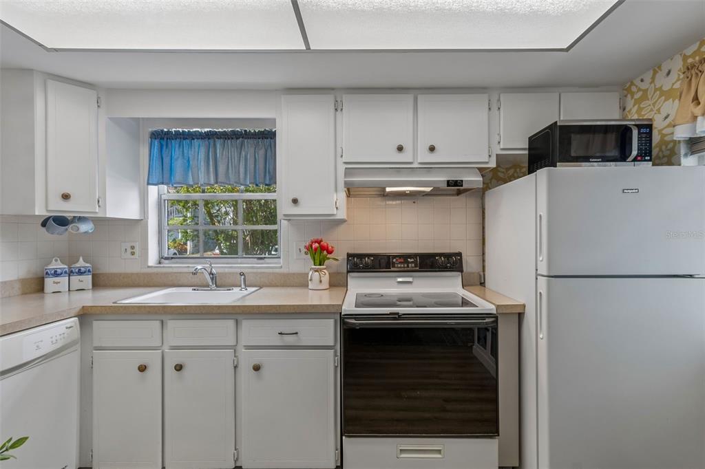 A kitchen features white cabinets, a white stove, a refrigerator, and a window above the sink — 200 GLENNES LANE UNIT 112, DUNEDIN, FL