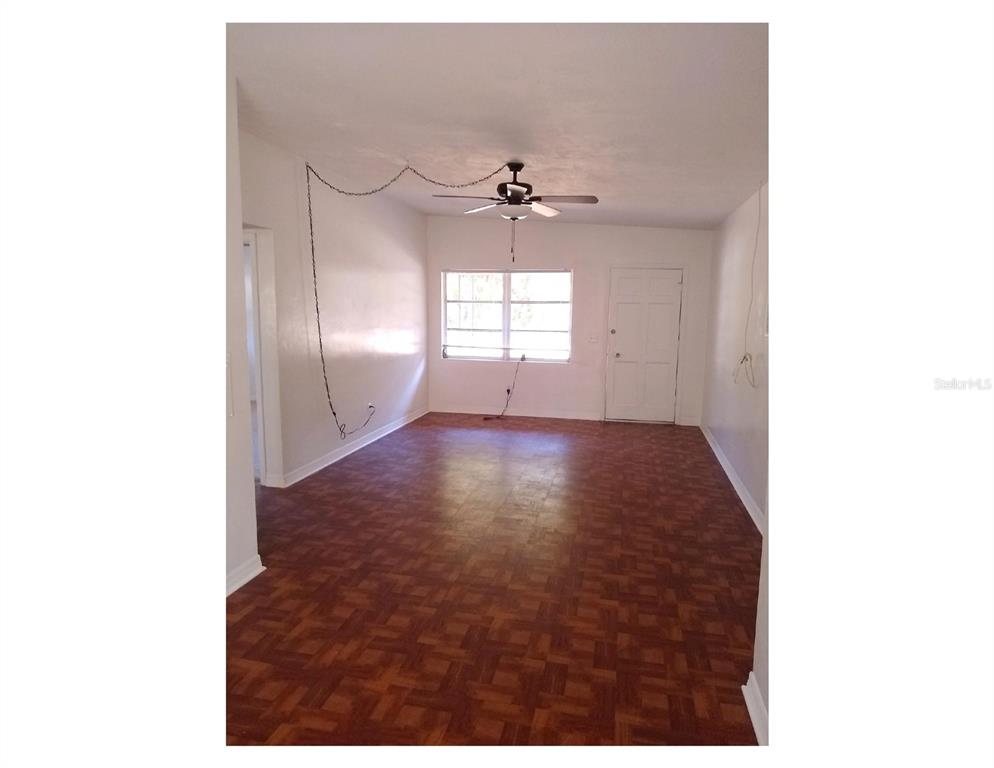 An empty room features parquet wood flooring, a ceiling fan, and a white front door — 446 NEW YORK AVENUE, DUNEDIN, FL