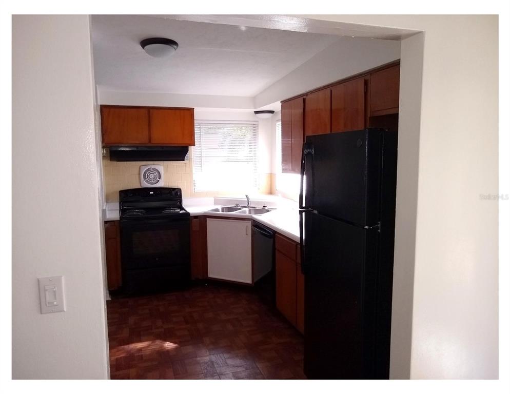 A kitchen features wood cabinets, black appliances, a corner sink, and parquet flooring — 446 NEW YORK AVENUE, DUNEDIN, FL