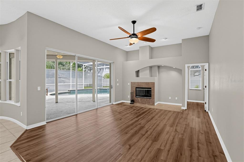 A living room with wood-look flooring, a fireplace, a ceiling fan, and sliding glass doors — 248 HUNTRIDGE WAY, WINTER SPRINGS, FL
