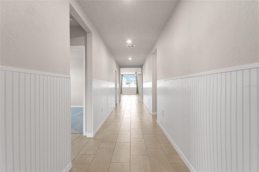 A long hallway with light-colored tile flooring and white wainscoting on the walls — 1355 BENEVENTO DRIVE, WINTER HAVEN, FL