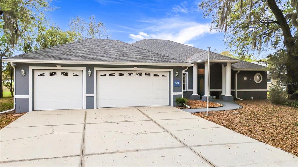 A gray single-story house with a three-car garage and a paved driveway — 507 DOWLING CIRCLE, LADY LAKE, FL