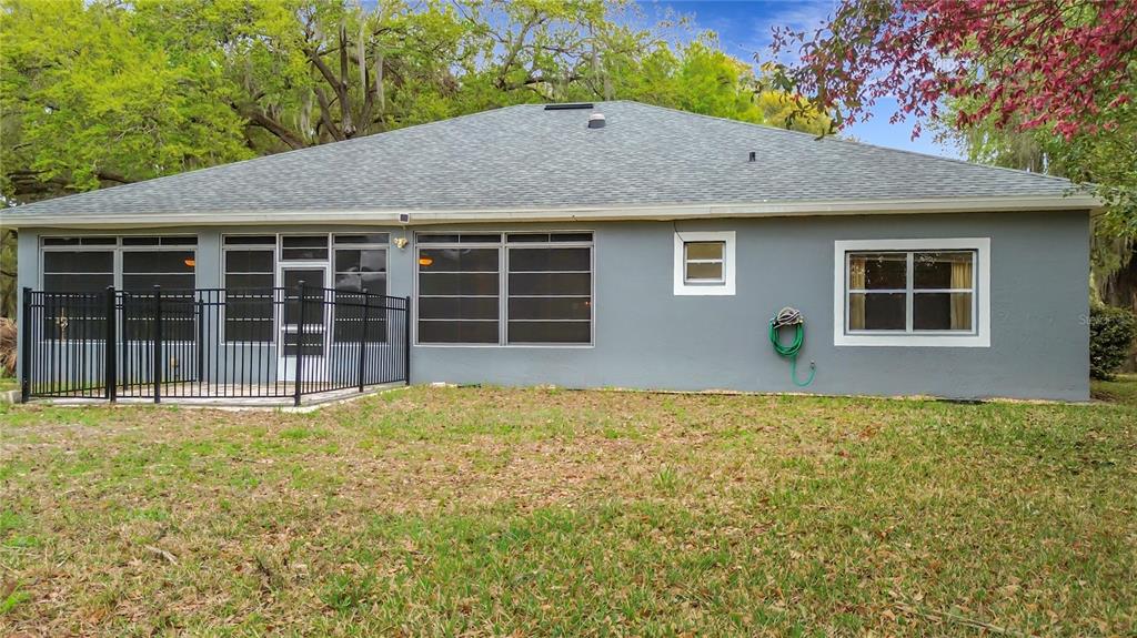The rear exterior of a gray house features a screened-in porch and a fenced patio — 507 DOWLING CIRCLE, LADY LAKE, FL
