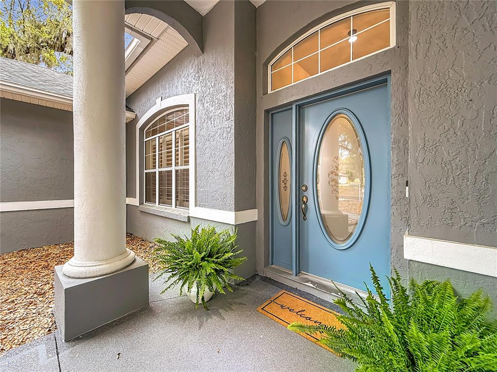 A blue front door with an oval glass insert sits under a covered entryway — 507 DOWLING CIRCLE, LADY LAKE, FL