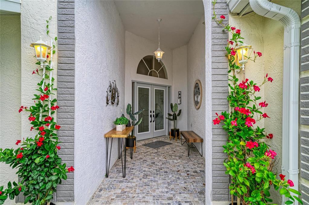 A covered entryway features a tiled floor, double glass doors, and climbing vines with red flowers — 6604 STONE RIVER ROAD, BRADENTON, FL