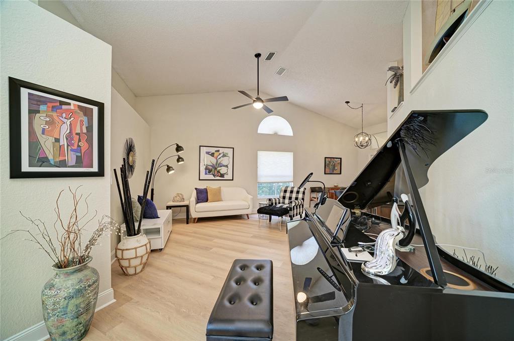 A living room with a grand piano, light wood floors, and vaulted ceilings — 6604 STONE RIVER ROAD, BRADENTON, FL