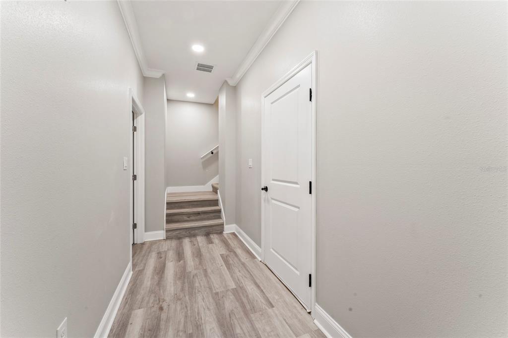 A hallway with light wood-look flooring leads to a short staircase and a white door — 809 W LINEBAUGH AVE UNIT 2A, TAMPA, FL
