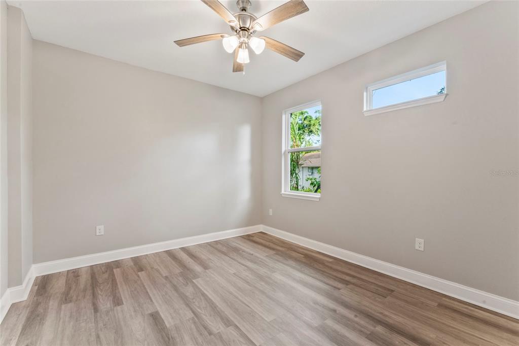An empty room features light gray walls, wood-look flooring, a ceiling fan, and two windows — 809 W LINEBAUGH AVE UNIT 2A, TAMPA, FL