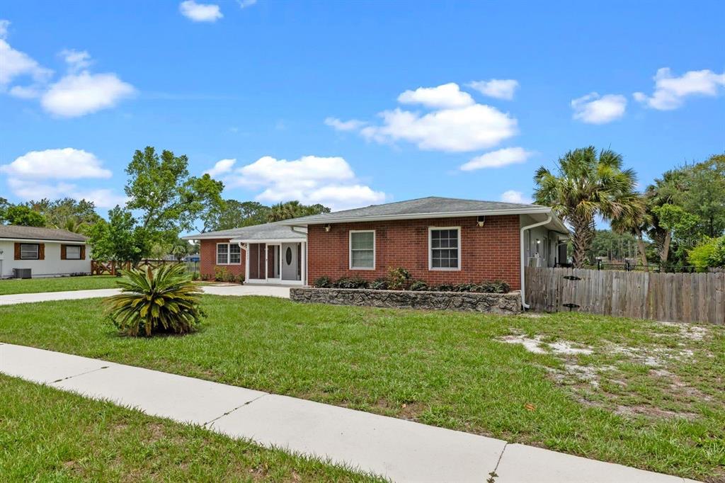 A single-story brick house with a concrete driveway and a wooden fence under a blue sky — 2622 HIBISCUS COURT, DELTONA, FL