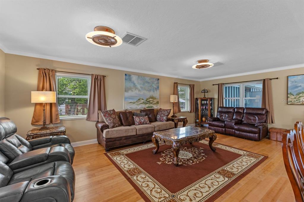 A living room features hardwood floors, a brown area rug, leather furniture, and ceiling fans — 2622 HIBISCUS COURT, DELTONA, FL