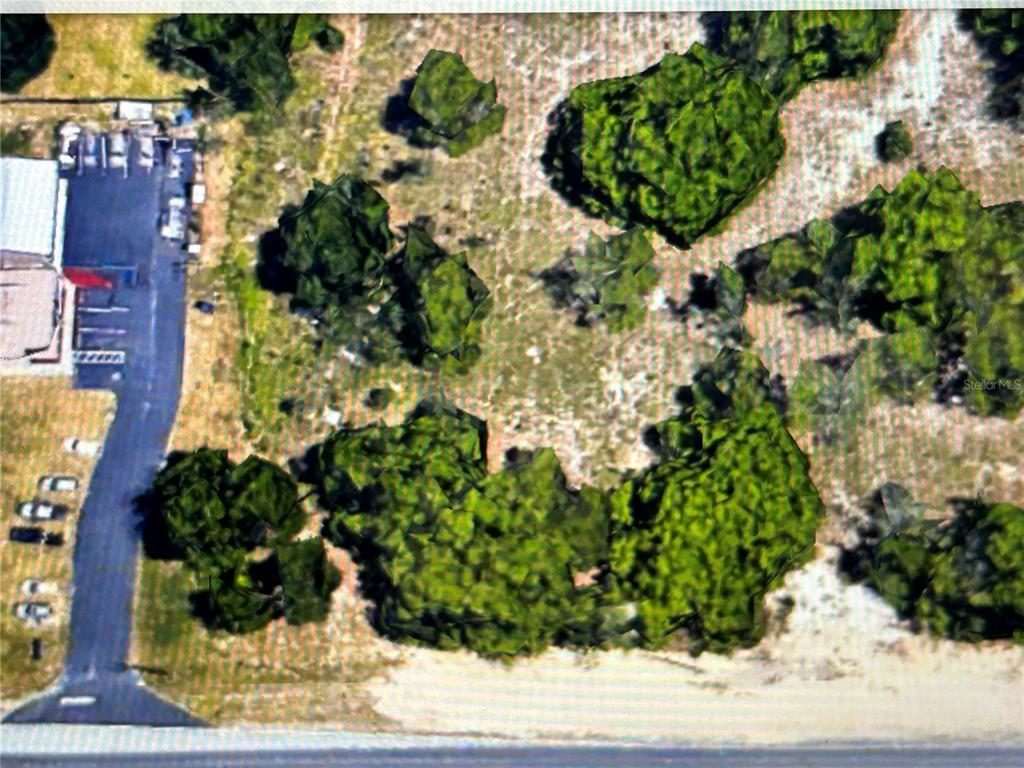 An aerial view shows a paved driveway leading to a building beside a wooded lot — COUNTYLINE, SPRING HILL, FL