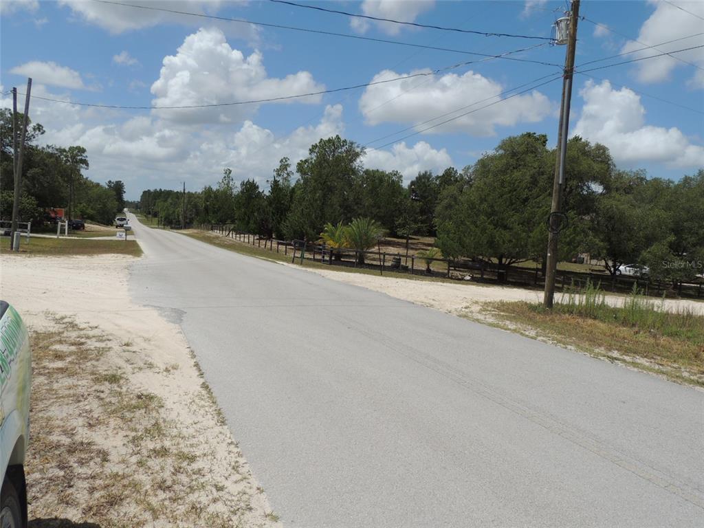 A paved road stretches into the distance past a fenced property with trees and utility poles — 13591 NE 51ST LANE, WILLISTON, FL