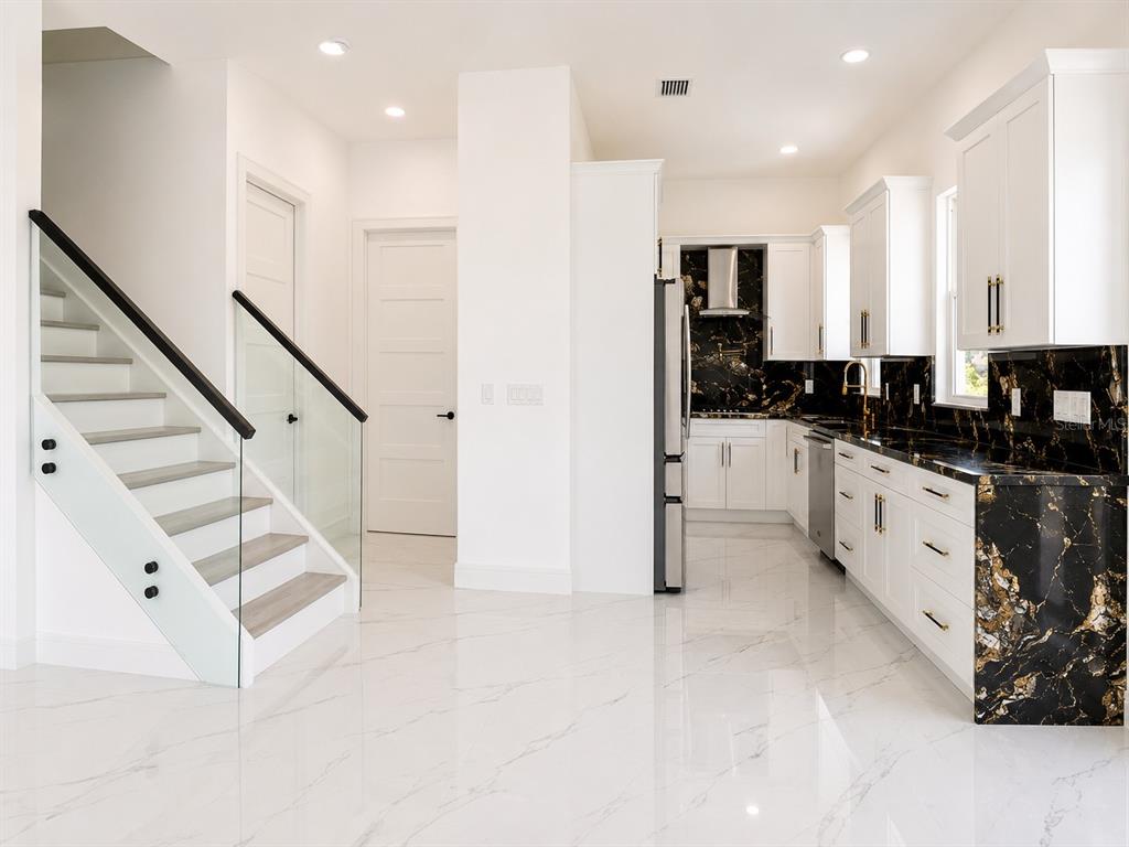 An open-concept living area features white marble-look tile floors, a glass-railed staircase, and sliding doors — 6510 SIMONE SHORES CIR, APOLLO BEACH, FL