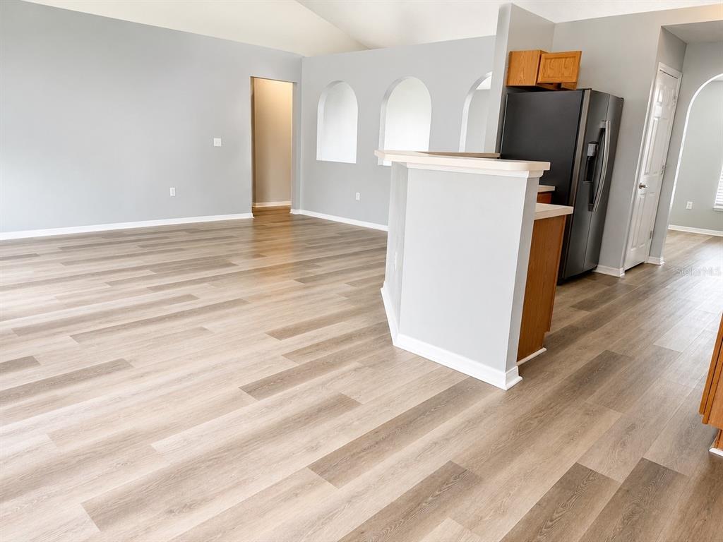 A kitchen with wood cabinets, light countertops, and grey wood-look flooring leads to an archway — 3080 UTAH DRIVE, DELTONA, FL