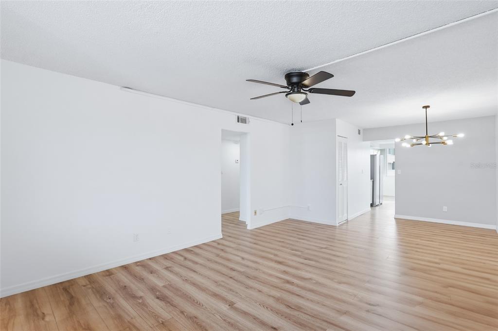 An empty room with light wood-look flooring, white walls, a ceiling fan, and a chandelier — 5095 BAY STREET NE UNIT 210, ST PETERSBURG, FL