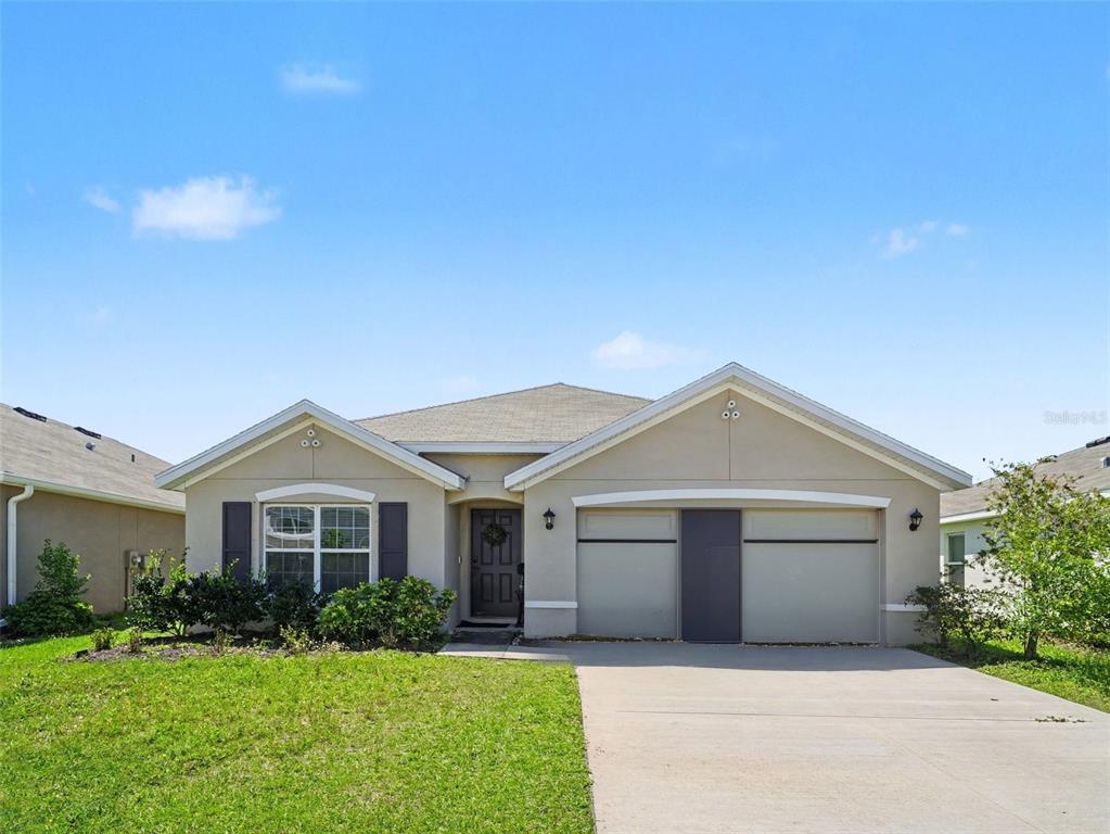 A single-story house with a beige stucco exterior, a two-car garage, and a front lawn — 12151 KINGSLEY TRAIL, PARRISH, FL
