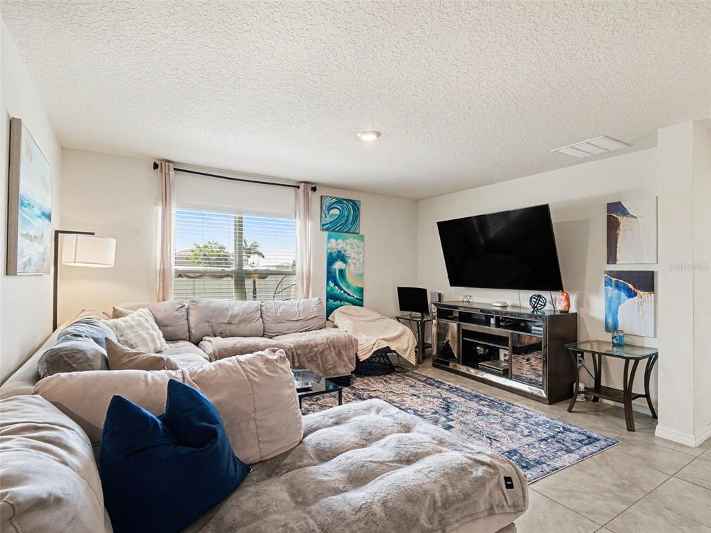 A living room features a large sectional sofa, a wall-mounted television, and blue-themed wall art — 12151 KINGSLEY TRAIL, PARRISH, FL
