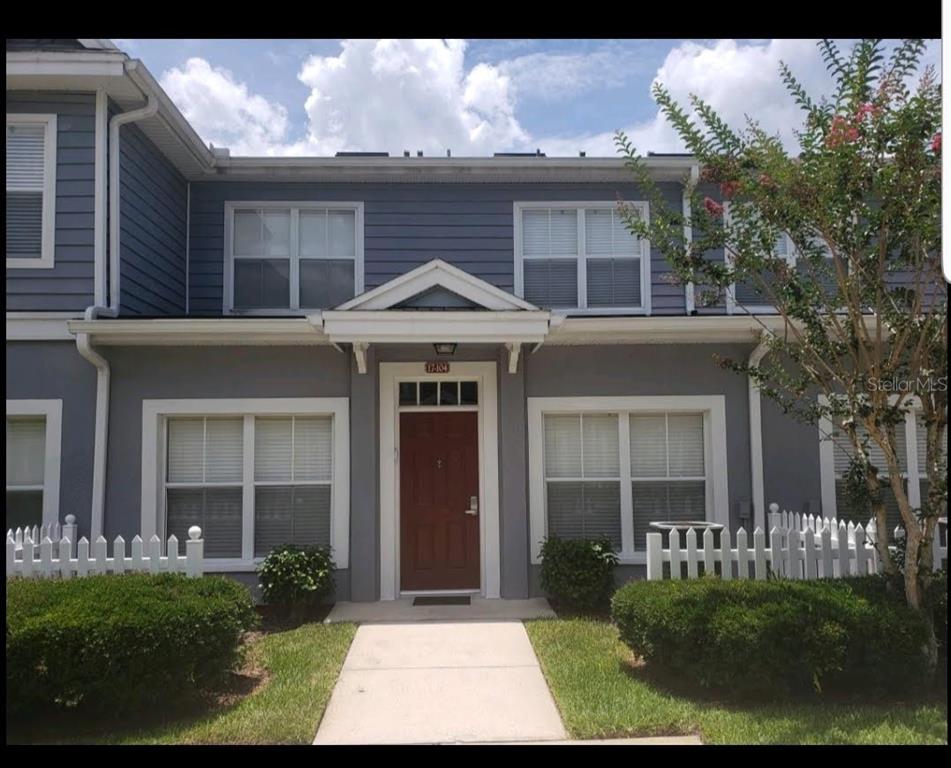 A two-story townhouse exterior features a red front door, gray siding, and a white fence — 4562 JONAFREE LANE UNIT 104, KISSIMMEE, FL