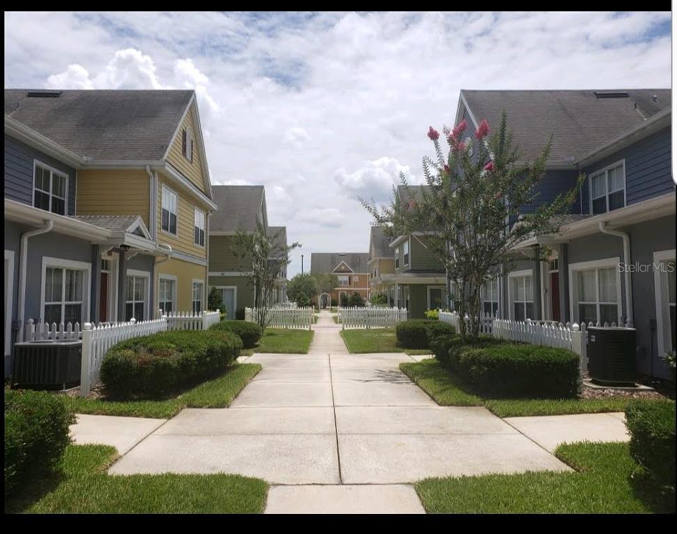 A concrete walkway leads between two rows of colorful townhomes with white picket fences — 4562 JONAFREE LANE UNIT 104, KISSIMMEE, FL