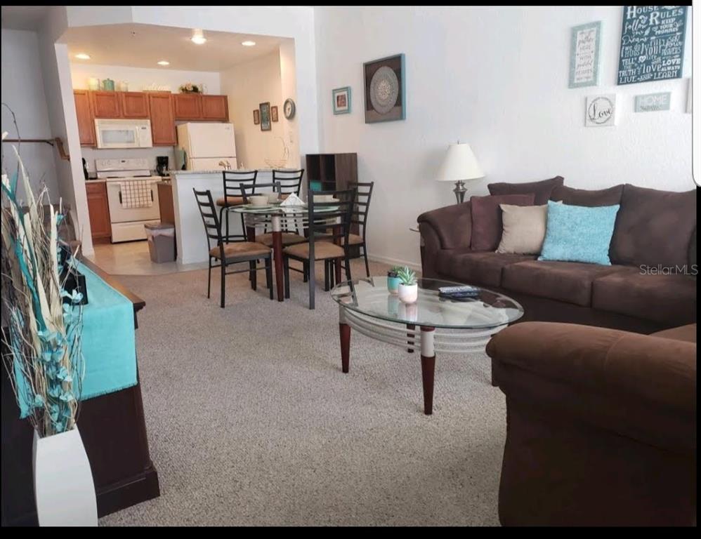 An open-concept living room with a brown sofa, glass coffee table, and adjacent dining area — 4562 JONAFREE LANE UNIT 104, KISSIMMEE, FL