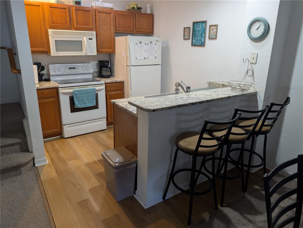 A kitchen features wood cabinets, white appliances, a granite breakfast bar, and three bar stools — 4562 JONAFREE LANE UNIT 104, KISSIMMEE, FL