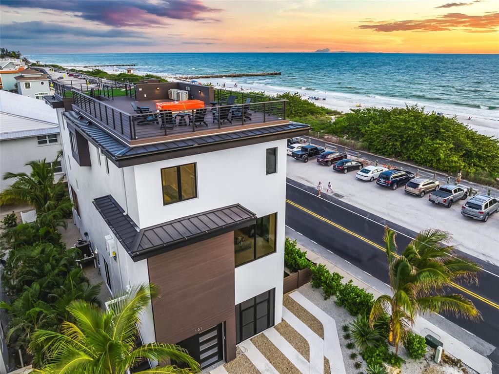 An aerial view shows a modern three-story house with a rooftop deck overlooking the ocean — 101 7TH STREET S, BRADENTON BEACH, FL