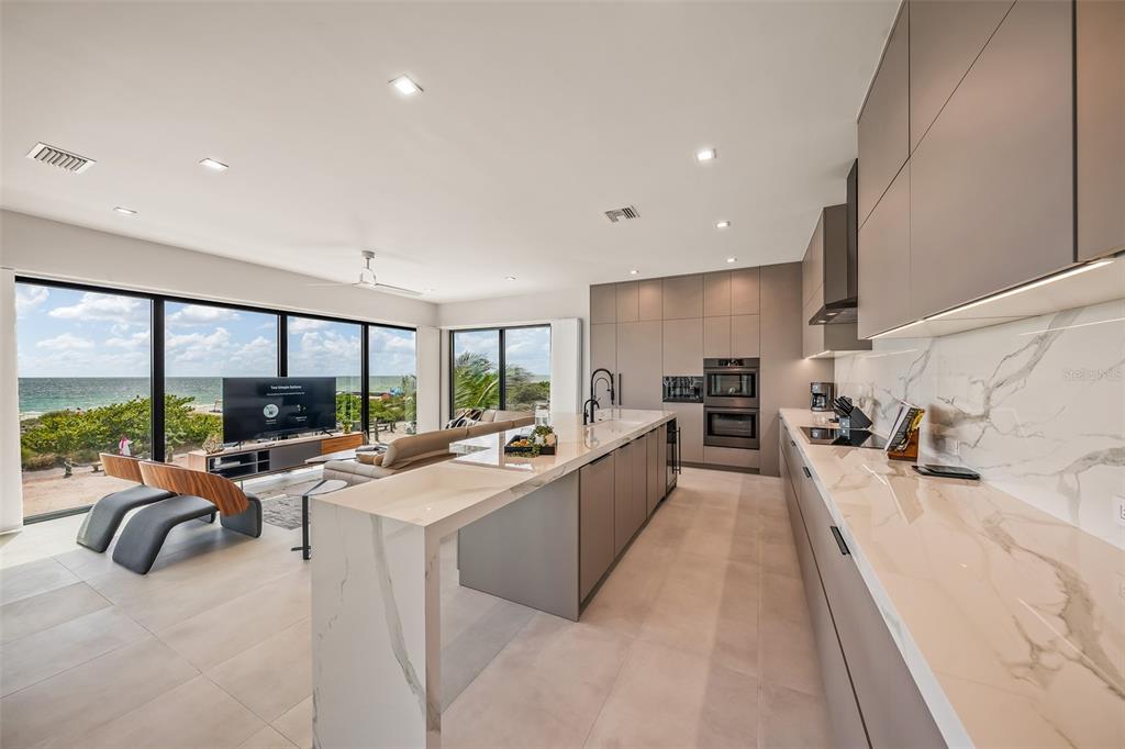A modern kitchen with marble countertops and gray cabinetry overlooks a beach and ocean view — 101 7TH STREET S, BRADENTON BEACH, FL