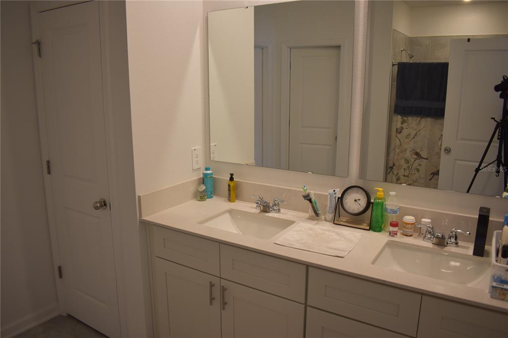 A bathroom features a double vanity with white cabinets, light countertops, and a large mirror — 1406 DEEPWATER CIRCLE, EAGLE LAKE, FL