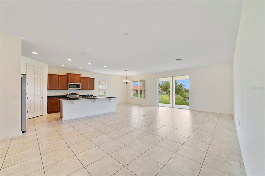 An open-concept kitchen and living area with tile flooring, wooden cabinets, and sliding glass doors — 3880 CARRICK BEND DRIVE, KISSIMMEE, FL