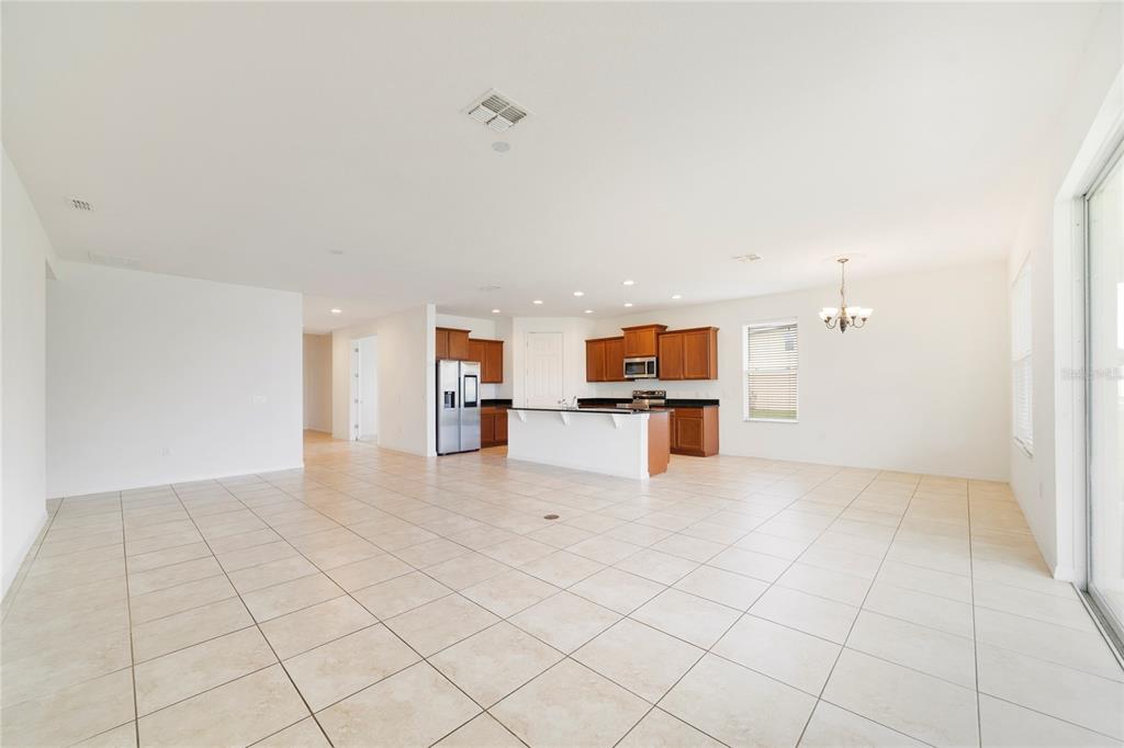 An open-concept kitchen with wood cabinets and a white island overlooks a tiled living area — 3880 CARRICK BEND DRIVE, KISSIMMEE, FL