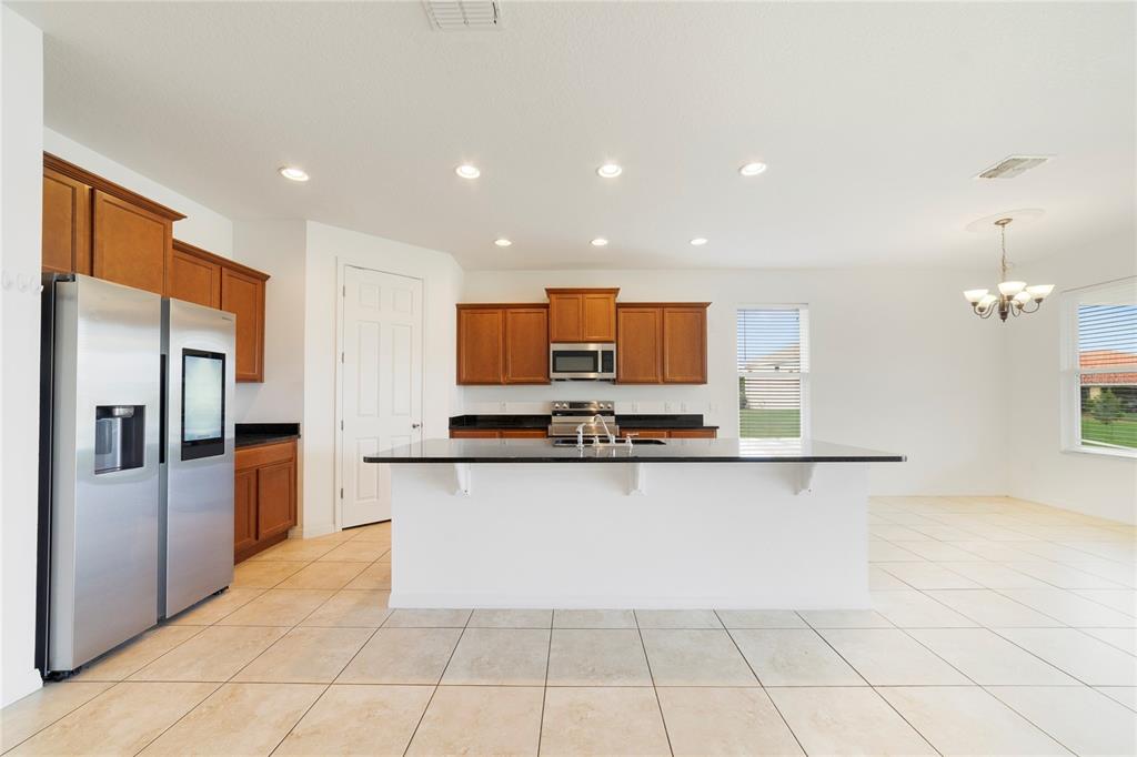 A kitchen features wood cabinets, black countertops, a central island, and light-colored tile flooring — 3880 CARRICK BEND DRIVE, KISSIMMEE, FL